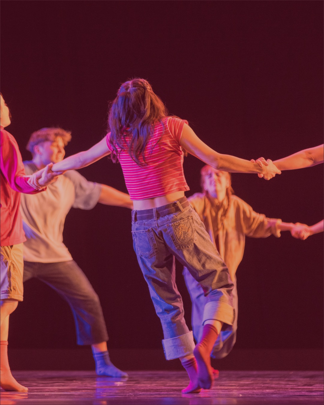 students stand onstage joyously holding hands in dance